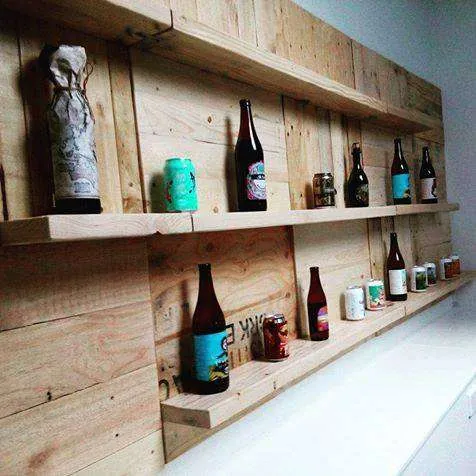 Recycled pallet timber shelving stacked with bottles behind a bar